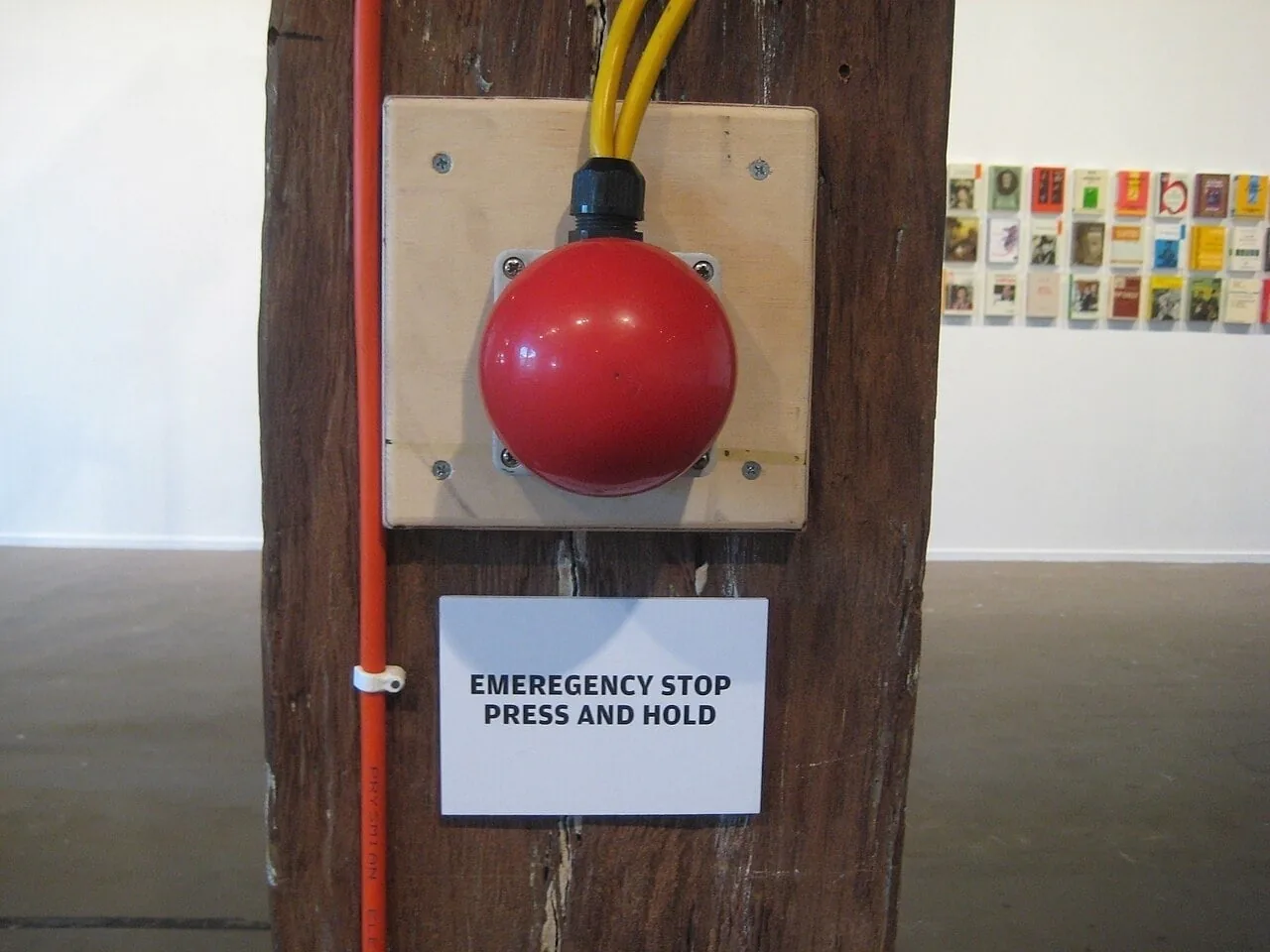 A red emergency stop button on a wooden post with a sign reading: emergency stop, press and hold.